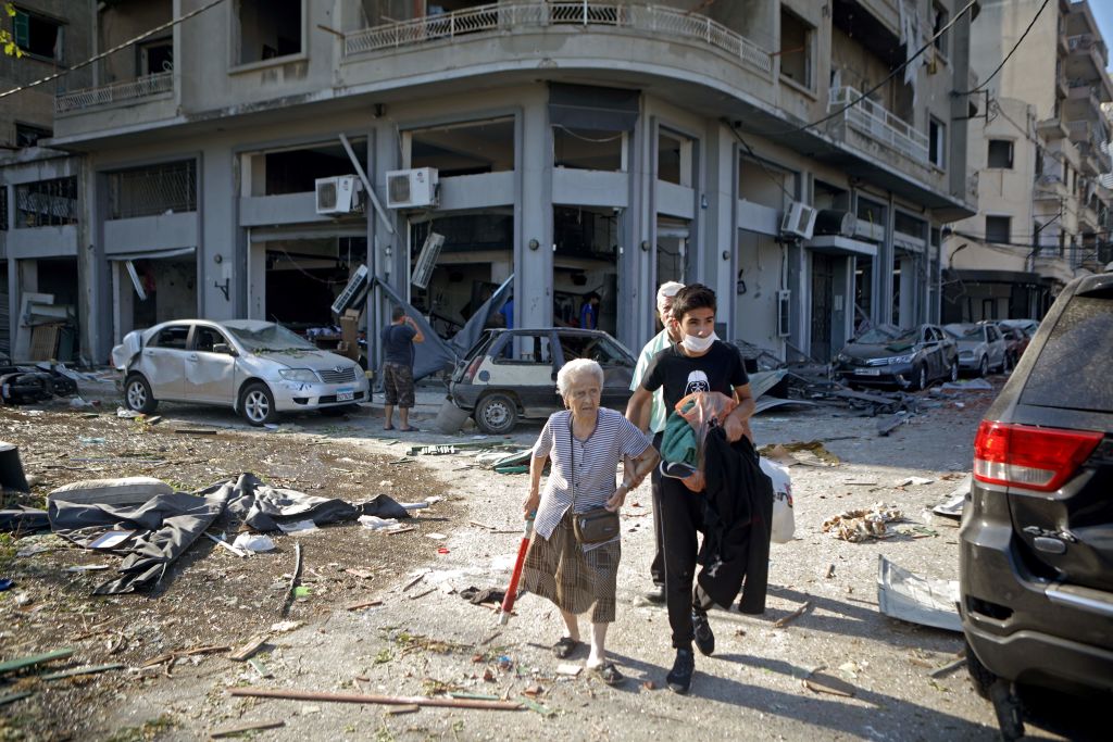 PATRICK BAZ/AFP via Getty Images - A older woman is helped away from the rubble in Beirut after the explosion.